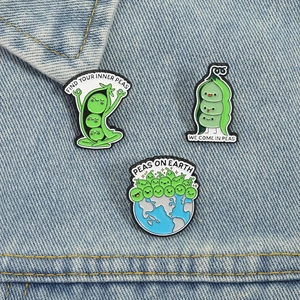 Three cute green pea enamel pins with funny puns displayed on denim fabric background
