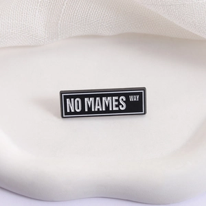 Rectangle black enamel brooch featuring bold white NO MAMES WAY text on a stone tray