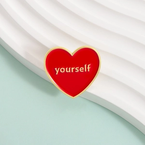Détail d'une épingle cœur en émail rouge avec bord doré et lettrage yourself en relief