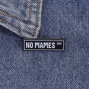 Macro detail of enamel pin with NO MAMES WAY text pinned on blue denim jacket fabric