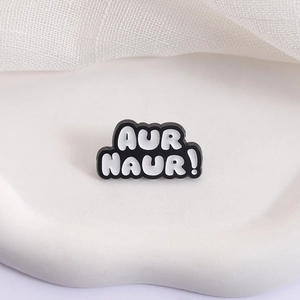 Minimalist black and white enamel AUR NAUR! metal badge brooch on a white display tray
