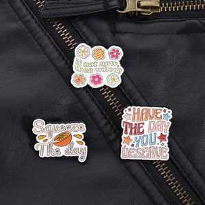 Three inspirational enamel pins with motivational quotes pinned on a black leather jacket