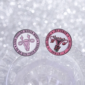Empowering pink uterus enamel pins with floral patterns on a reflective glass surface