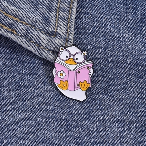 Gros plan d'un pin's en émail canard blanc lisant un livre rose sur du denim