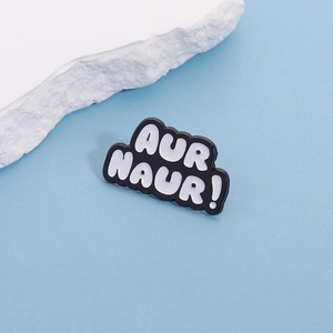 Macro shot of black enamel pin with white 'AUR NAUR!' lettering on blue background