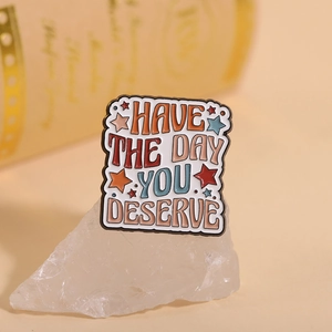Macro shot of an enamel pin featuring Have The Day You Deserve text with colorful stars