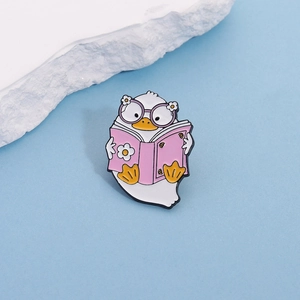 Cute white duck enamel pin with purple glasses reading a book on a light blue background