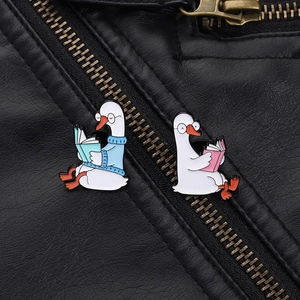 Detail of two cute geese enamel pins with glasses reading books on a black leather jacket