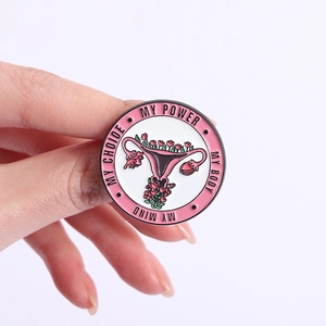 Gros plan détaillé d'un pin's féministe rond en émail avec utérus fleuri et slogan