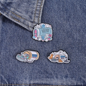 Drei Emaille-Pins mit Katzen- und Hundemedizin-Themen auf blauem Denim-Hintergrund