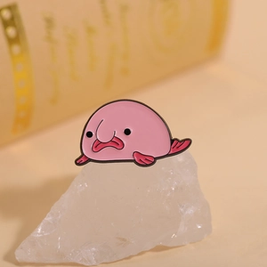 Macro shot of a pink blobfish enamel pin resting on white crystal stone with blurred background