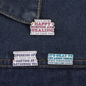 Nahaufnahme von Emaille-Pins mit Zitaten auf blauem Jeansstoff Hintergrund