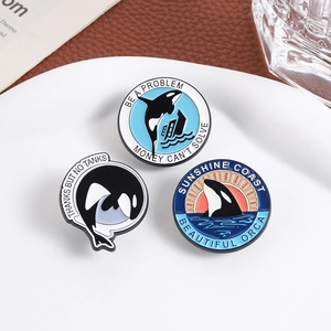 Orca whale enamel pins set featuring three diverse designs on a clean ceramic plate