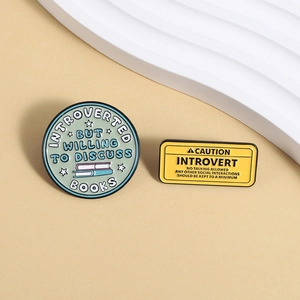 Detail view of two enamel pins with humorous introvert and book lover quotes