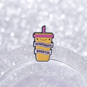 Macro shot of Serotonin Booster enamel pin resting on a glass edge with bokeh effect