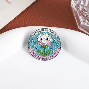 Enamel dandelion brooch featuring Hanging In There text and pink ribbon details