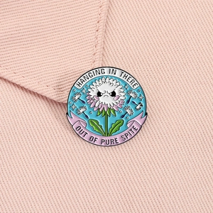 Detail of angry dandelion enamel pin with text Hanging in there out of pure spite