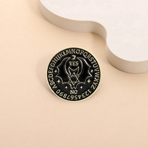 Detailed macro of a black and gold enamel Ouija pin with bat wings and starry patterns