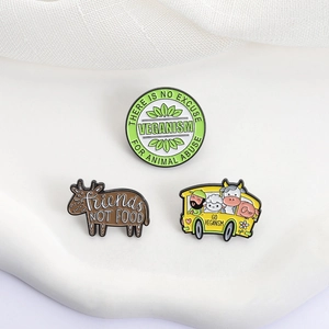 Detailed close-up of three vegan theme enamel pins on a soft white wave background