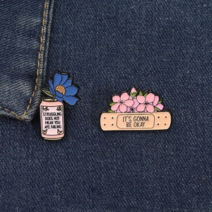 Détail de broches en émail fleuries avec citations sur fond en jean bleu foncé