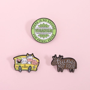 Detailed close-up of three vegan enamel pins with animal rights slogans on pink background