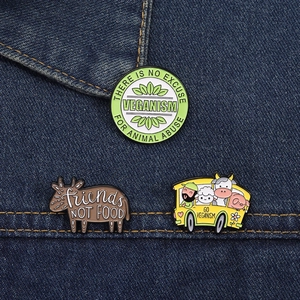 Detailed view of three vegan-themed enamel pins pinned on dark blue denim fabric