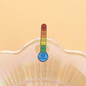 Detail view of colorful enamel thermometer mood pin with emoji icons on a shell tray