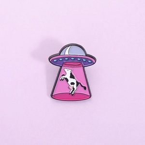 Broche créative en émail d'un OVNI violet enlevant une vache sur fond lilas pastel