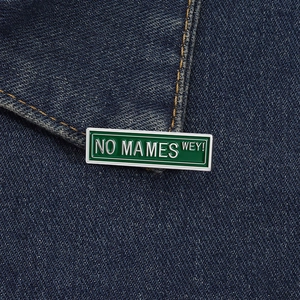 Dettaglio della spilla in smalto verde NO MAMES WEY appuntata su tessuto denim blu