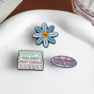Gros plan de trois épinglettes en émail pastel avec phrases motivantes sur plateau