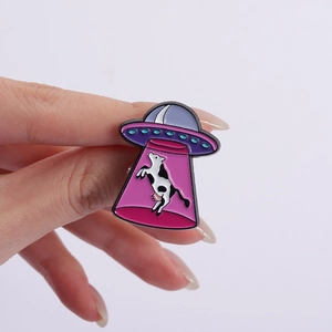 Vue détaillée du pin's émaillé OVNI violet avec vache tenue en main pour l'échelle