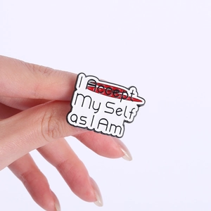 Detail shot of hand-held metal pin badge featuring I Accept My Self as I Am text