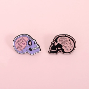 Close-up of enamel skull brooches with pastel pink brain details and funny engraved quotes