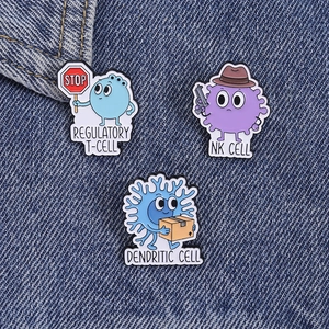 Detailed view of three cartoon enamel pins depicting immune cells on blue denim fabric