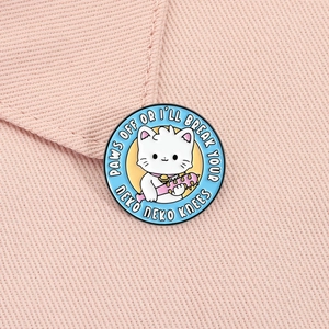 Gros plan d'un pin's en émail bleu avec chat de dessin animé sur tissu rose texturé