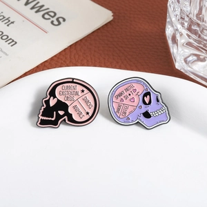 Detailed close-up of two skull enamel pins with creative lettering on a white ceramic plate