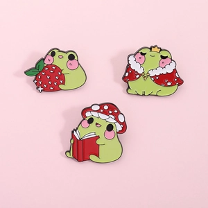 Detailed view of three cute frog enamel pins with strawberry and mushroom motifs
