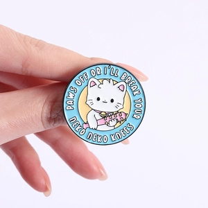 Détail d'un pin's chat en émail avec une masse d'armes tenu en main pour montrer la taille