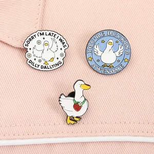 Detailed view of three cute cartoon duck enamel pins with funny slogans on pink fabric