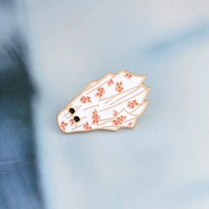 Macro shot of cute ghost enamel pin with pink floral pattern and gold metal plating
