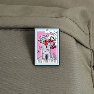 Pink tarot enamel pin featuring XVI The Patriarchy design on green fabric texture