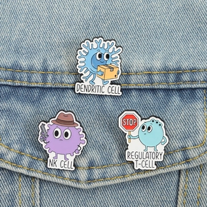 Three cartoon science biology enamel pins featuring immune cells on a denim jacket pocket