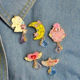 Pink and yellow enamel brooches with heart and wing designs on denim fabric