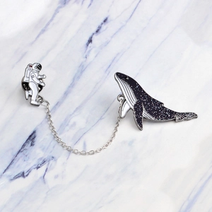 Detailed view of astronaut and starry whale enamel pin with a delicate silver metal chain