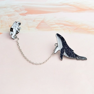 Close-up of enamel astronaut and whale pin set connected by a silver chain
