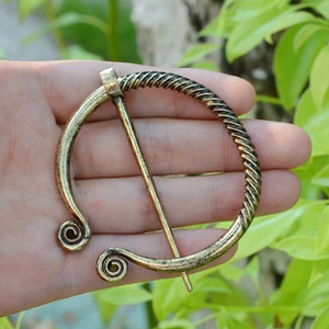 Vue macro d'une broche fibule viking vintage en métal bronze tenue dans une main