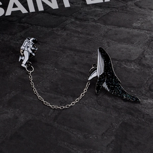 Detailed view of astronaut and starry whale enamel brooches linked by a metal chain
