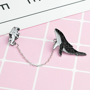 Detail of enamel astronaut and whale brooch set with metal chain on pink grid background