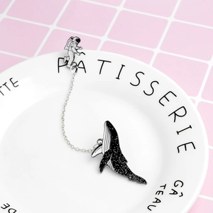 Detailed view of enamel astronaut and whale chain brooch on a white porcelain dish