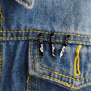 Detail of three black and white punk rose enamel pins pinned on a blue denim jacket pocket